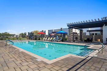 A resort style pool with lounge chairs and umbrellas next to a building